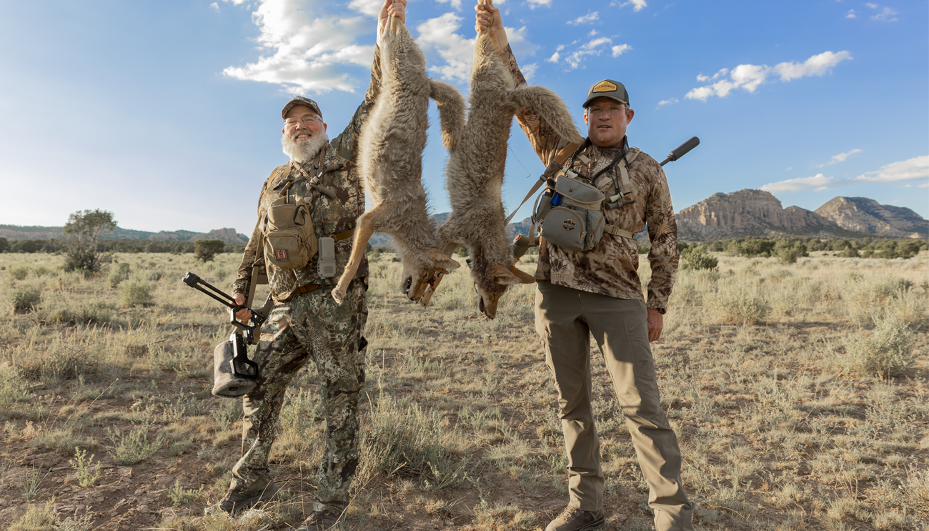 Two hunters each holding a harvested coyote.